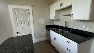 Kitchen with dark stone counters, white cabinetry, and dishwasher