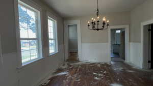 Unfurnished dining area featuring a wainscoted wall, a chandelier, and wood-type flooring