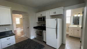 Kitchen with appliances with stainless steel finishes, white cabinets, and light tile patterned floors