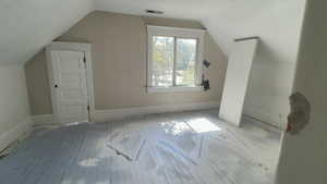 Additional living space with a textured ceiling, hardwood / wood-style floors, and vaulted ceiling