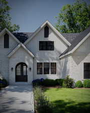 View of front of home featuring brick siding, a shingled roof, a front yard, and french doors
