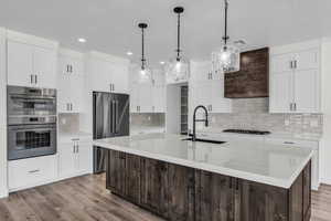 Kitchen featuring dark brown cabinetry, white cabinetry, an island with sink, hanging light fixtures, and recessed lighting