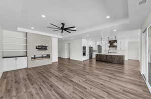 Unfurnished living room featuring a tray ceiling, a large fireplace, dark wood-style floors, a ceiling fan, and recessed lighting