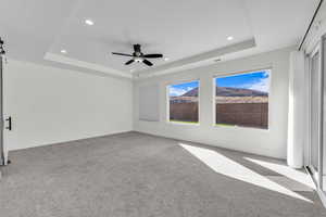 Unfurnished room with a tray ceiling, light colored carpet, a barn door, recessed lighting, and ceiling fan