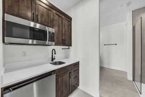 Kitchen featuring dark brown cabinetry, appliances with stainless steel finishes, and light stone counters