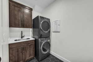 Laundry area featuring dark tile patterned floors, stacked washer and clothes dryer, and cabinet space
