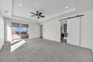 Unfurnished bedroom with a raised ceiling, access to outside, a barn door, carpet flooring, and recessed lighting