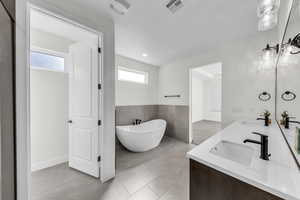 Bathroom with a freestanding tub, tile walls, double vanity, a wainscoted wall, and light tile patterned flooring