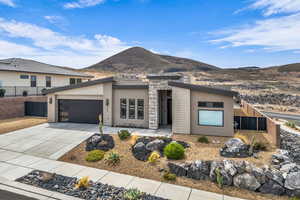 Contemporary home with concrete driveway, stucco siding, an attached garage, a mountain view, and stone siding