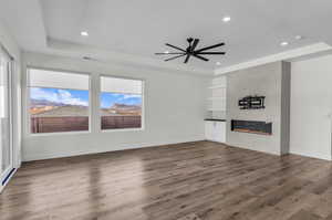 Unfurnished living room with a raised ceiling, wood finished floors, a tile fireplace, recessed lighting, and ceiling fan