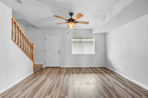 Living room with light wood-style flooring, ceiling fan, and stairs leading up to 2nd story