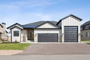Modern inspired farmhouse featuring board and batten siding, a garage, driveway, and a front lawn