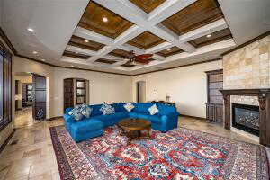 Living area featuring arched walkways, coffered ceiling, beamed ceiling, a glass covered fireplace, and ornamental molding