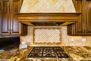 Kitchen featuring premium range hood, backsplash, dark stone countertops, and stainless steel gas stovetop