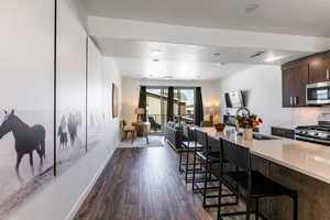 Kitchen featuring appliances with stainless steel finishes, backsplash, open floor plan, dark wood-style floors, and dark brown cabinets