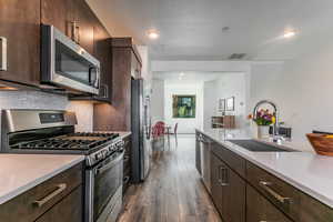 Kitchen featuring dark brown cabinets, stainless steel appliances, light stone countertops, dark wood finished floors, and a textured ceiling