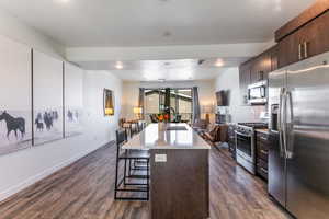 Kitchen with dark brown cabinetry, appliances with stainless steel finishes, a breakfast bar area, dark wood-type flooring, and recessed lighting