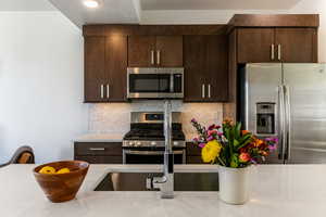 Kitchen featuring tasteful backsplash, appliances with stainless steel finishes, dark brown cabinetry, a textured ceiling, and light stone countertops