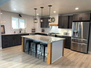 Kitchen featuring appliances with stainless steel finishes, tasteful backsplash, a breakfast bar area, light stone countertops, and recessed lighting