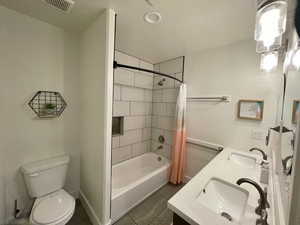 Bathroom with shower / tub combo, dark tile patterned flooring, and double vanity