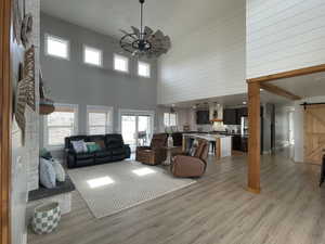 Living area featuring a barn door, a towering ceiling, light wood-type flooring, plenty of natural light, and a ceiling fan