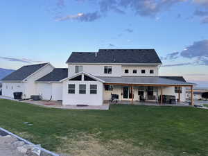 Back of property at dusk with a patio and a yard