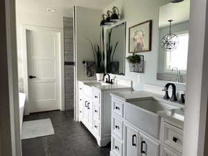 Full bathroom featuring two vanities, a soaking tub, dark tile patterned floors, and a chandelier