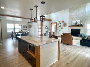 Kitchen featuring hanging light fixtures, light stone counters, light wood finished floors, a stone fireplace, and a textured ceiling
