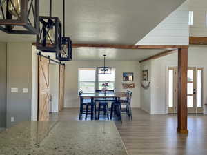 Dining room featuring a barn door, light wood-style floors, a textured ceiling, a chandelier, and beam ceiling