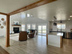 Living room featuring light wood-style floors, a fireplace, a towering ceiling, beamed ceiling, and brick wall