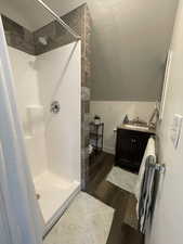 Bathroom featuring vanity, a shower stall, dark wood-style flooring, and lofted ceiling