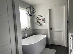 Full bath featuring a freestanding bath, tile walls, vanity, dark tile patterned floors, and wainscoting