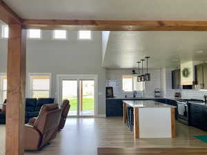 Kitchen featuring decorative backsplash, gas stove, hanging light fixtures, light stone counters, and beamed ceiling