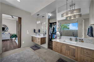 Bathroom with two vanities, a walk in closet, light tile patterned floors, and backsplash