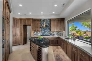 Kitchen featuring recessed lighting, tasteful backsplash, dark stone counters, wall chimney exhaust hood, and a center island