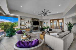 Tiled living room with ceiling fan, recessed lighting, a stone fireplace, and a tray ceiling