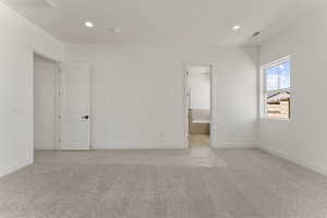 Unfurnished bedroom with light colored carpet, recessed lighting, and connected bathroom