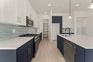 Kitchen with white cabinets, tasteful backsplash, appliances with stainless steel finishes, blue cabinetry, and recessed lighting