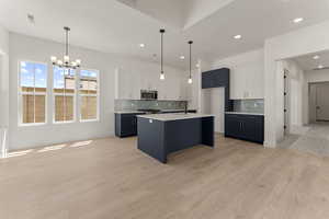 Kitchen featuring white cabinets, a chandelier, hanging light fixtures, backsplash, and a center island with sink