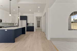 Kitchen with pendant lighting, white cabinetry, tasteful backsplash, light wood-type flooring, and a center island with sink
