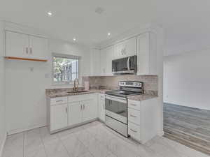 Kitchen featuring stainless steel appliances, white cabinets, decorative backsplash, light stone countertops, and recessed lighting