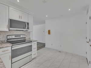 Kitchen featuring appliances with stainless steel finishes, white cabinetry, light stone counters, recessed lighting, and decorative backsplash