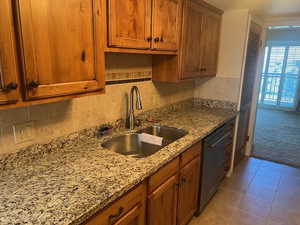 Kitchen featuring backsplash, brown cabinets, light tile patterned flooring, light stone countertops, and light carpet
