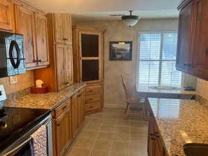 Kitchen featuring stainless steel range with electric stovetop, light stone countertops, black microwave, light tile patterned floors, and brown cabinets