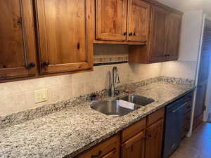 Kitchen with tasteful backsplash, light stone countertops, dishwasher, brown cabinets, and light tile patterned floors