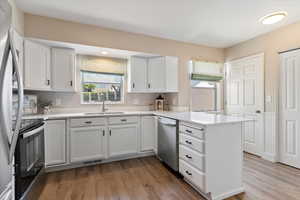 Kitchen with appliances with stainless steel finishes, white cabinets, a peninsula, and light wood finished floors