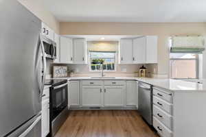 Kitchen featuring appliances with stainless steel finishes, light wood-style floors, white cabinets, and a peninsula