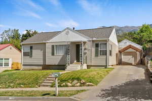 View of front facade with a shingled roof, an outdoor structure, a garage, driveway, and a front lawn