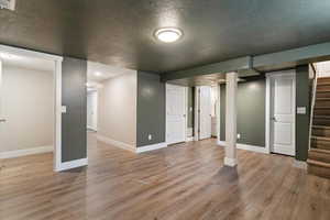 Finished basement featuring a textured ceiling, light wood finished floors, and stairway