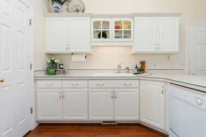 Kitchen with dishwasher, light countertops, white cabinetry, glass insert cabinets, and dark wood finished floors